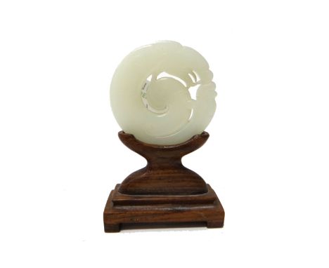 A Chinese white jade plaque, 19th/20th century, carved in the form of a chilong, 6cm. diameter, wood stand. 9