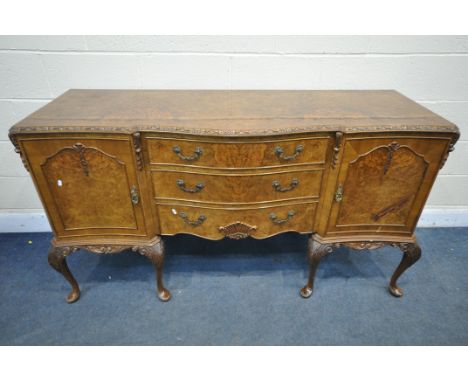 A REPRODUCTION QUEEN ANNE STYLE WALNUT SERPENTINE SIDEBOARD, with double cupboard doors, that's flanking three drawers, on ei