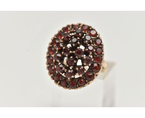 A 9CT GOLD GARNET DRESS RING, of a large oval openwork outline, set with circular cut garnets, approximate ring head measurin