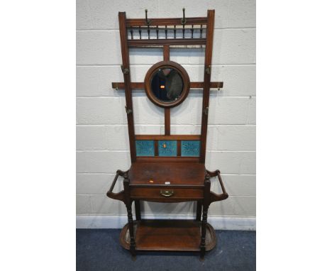 AN ARTS AND CRAFTS MAHOGANY HALL STAND, with six brass hooks, circular bevelled mirror, blue tiles, single drawer, and flanke