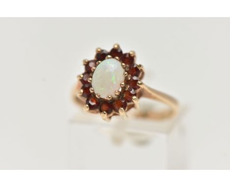 A 9CT GOLD OPAL AND GARNET CLUSTER RING, of an oval form, set with an oval cut opal cabochon claw set, in a surround of circu