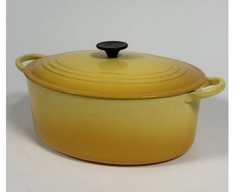 A Le Creuset oval cast iron casserole dish and cover with gradated yellow enamel finish, shows no signs of use. (H x 17 cm x 