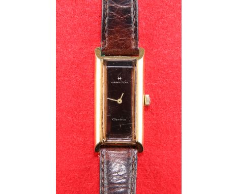A LADY'S GOLD-PLATED HAMILTON STRAP WATCH,&nbsp;rectangular brown dial with gilt hands, plain case, manual wind movement sign