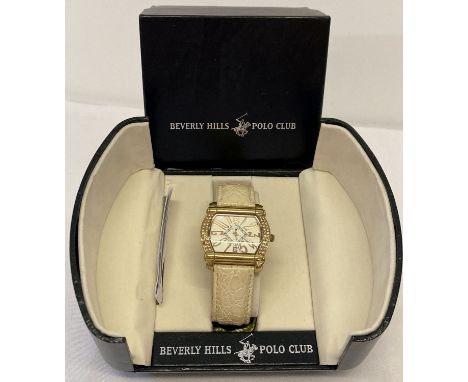 A boxed ladies Beverley Hills Polo Club wristwatch with square shaped face and cream leather strap.   Gold tone case set with
