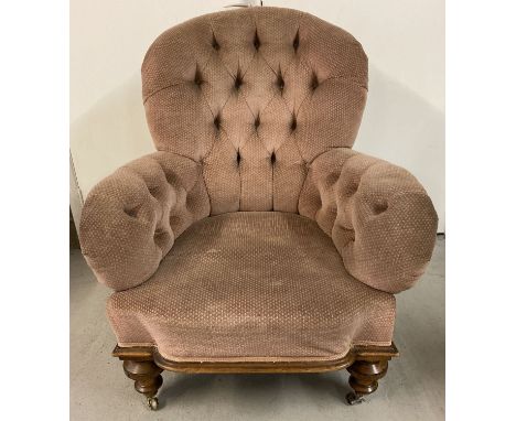 An Edwardian button back armchair with pale pink upholstery and castor feet.  One castor needs attention. 