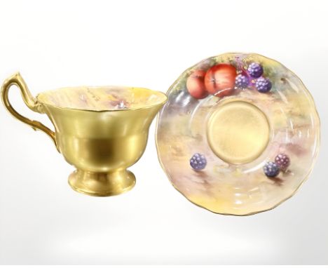 A Royal Worcester porcelain teacup and saucer, each hand-painted with panels of fruit, the teacup by R Austin, the saucer by 