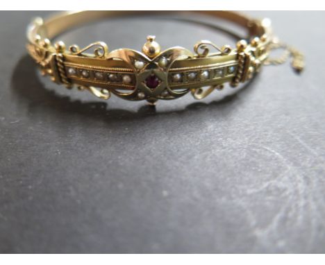 An Edwardian 9ct yellow gold bangle, push clasp with scrolled design and beading, set with a single mixed cut garnet and four