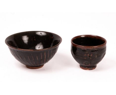 Jim Malone (born 1946) two footed stoneware bowls in tenmoku glaze, one with spiral fluting and a soft green flush to one sid