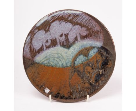 A round earthenware tile with contrasting purple and blue landscape design, DWB mark incised at edge, 19cm diameter
