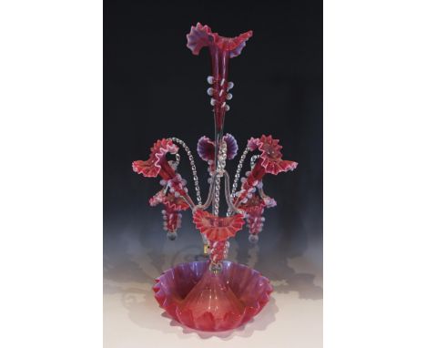 A cranberry glass epergne of typical form, with central trumpet over three lower trumpets, and three canes supporting hanging