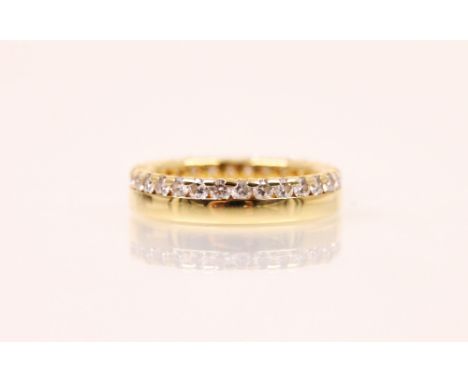 A diamond and yellow metal eternity ring, the continuous round cut diamonds claw and channel set above a plain polished band,