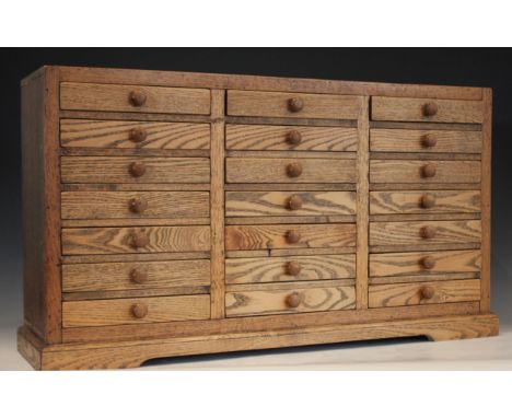 An oak specimen cabinet, 20th century, formed from three banks of seven small drawers, applied with button handles, upon a pl