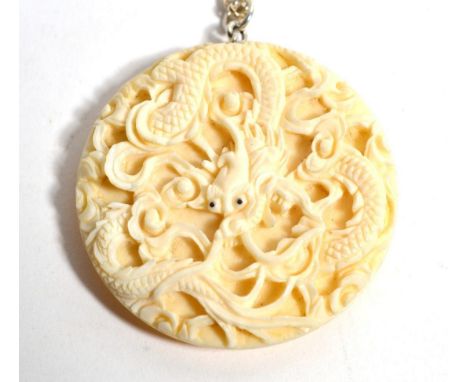 A Chinese ivory pendant/button, depicting a dragon, with an attached silver chain