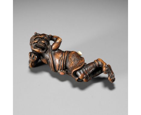 AN INLAID WOOD NETSUKE OF A RECLINING ONI AT SETSUBUNUnsigned Japan, 19th century, Edo period (1615-1868)A finely carved and 