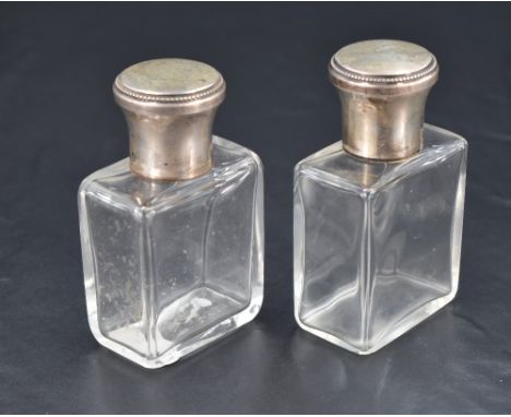 A pair of French white metal topped glass cologne or eau de toilette bottles, the screw-off covers of flared cylindrical form