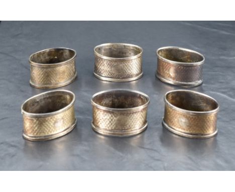 A group of six George V silver napkin rings, of oval form with engine-turned decoration and small vacant circular cartouches 