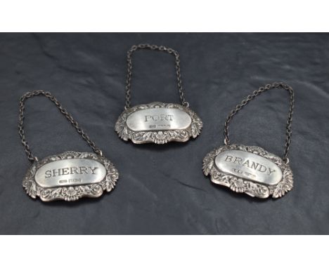 A group of three Queen Elizabeth II silver spirit labels, moulded with shells and scrolls, marked Port, Brandy and Sherry, ma