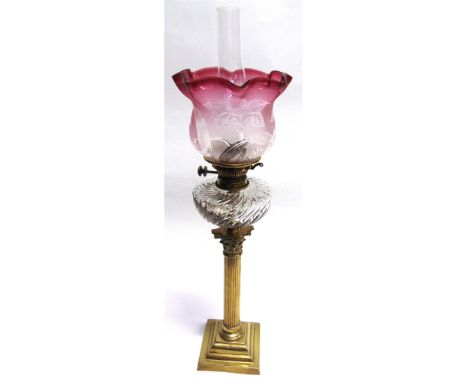 AN OIL LAMP WITH CRANBERRY GLASS SHADE  clear glass reservoir and brass Corinthian column base, 77cm high