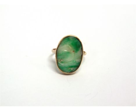AN EARLY 20TH CENTURY GOLD AND JADEITE RING the oval panel pierced and carved with fruits and leaves, rub-over set to a plain