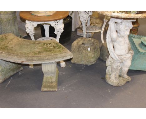 A WEATHERED COMPOSITE STONE GARDEN BENCH AND A WHITE PAINTED PUTTO FOUNTAIN