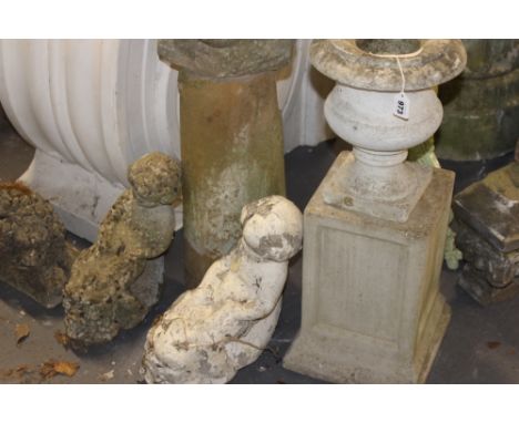 WEATHERED COMPOSITE STONE GARDEN ORNAMENTS. A RECUMBENT LION, TWO PUTTI FOUNTAIN SPOUTS AND A STONE URN ON A PLINTH