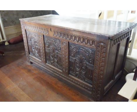 A CHARLES II OAK COFFER the plank top above a triple panelled front carved with architectural arcading and fleur de lis, with