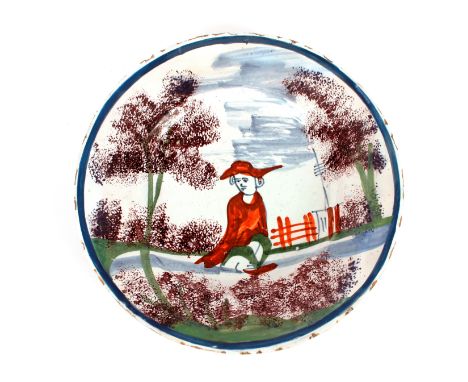A rare Bristol Delft plate, decorated in sponge ware with a seated male figure in a rural landscape wearing a red cloak and h