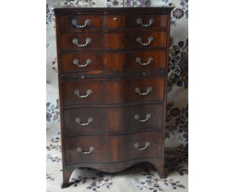 AN EARLY 20TH CENTURY MAHOGANY SERPENTINE CHEST OF SIX GRAUATED DRAWERS, with ornate brass handles and brushing slide, suppor