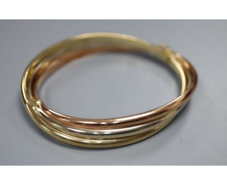 A 9ct three-colour gold bangle of oval, hollow, hinged design with overlapping bands, 18.1g