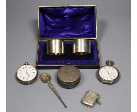 A cased pair of silver napkin rings, a silver pill box and spoon, a silver vesta case and two silver pocket watches.