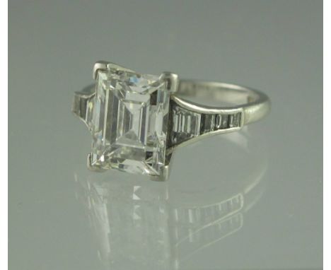 A STEP CUT DIAMOND RING. The stone an estimated 3.5cts with diamond set shoulders. Set in platinum. Ring size M.(B.P. 24% inc