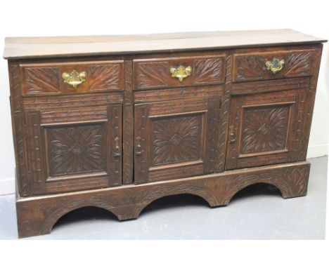 OAK DRESSER BASE having three frieze drawers over three blind panelled doors, overall with later foliate carving on a bracket