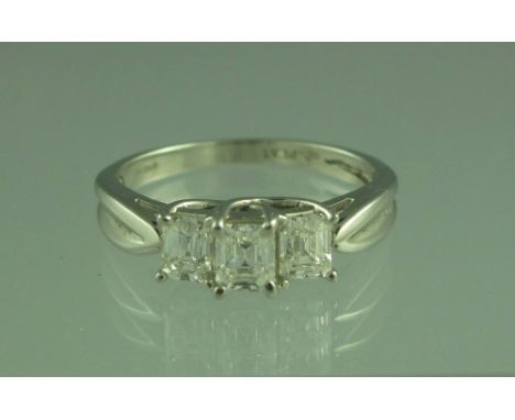 A PLATINUM AND DIAMOND THREE STONE RING. The three step cut diamonds claw set in a stepped mount. Ring size M.(B.P. 24% incl.