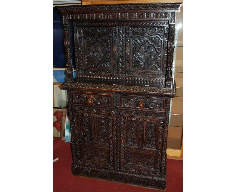 A late 19th century heavily carved and ebonised narrow oak court cupboard, the twin upper doors relief carved with royal port
