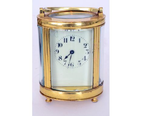 An early 20th Century French oval brass carriage clock with white enamelled dial and bevelled glass panel sides on cone feet,