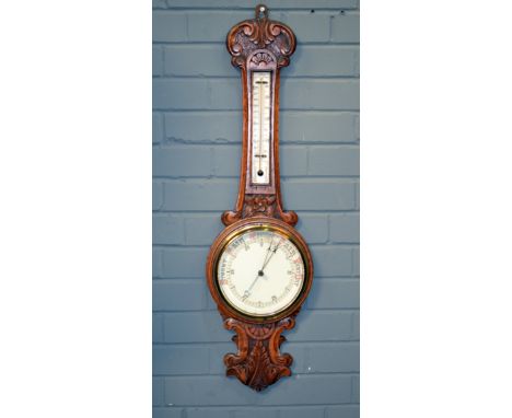 A late 19th to early 20th Century oak cased aneroid wheel barometer with carved scroll detail to the case. 
