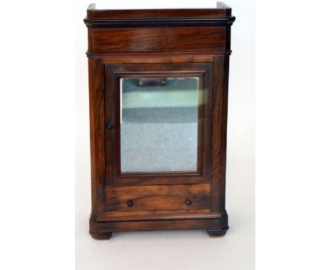 An early 20th Century miniature walnut apprentice armoire, the fitted shelf interior enclosed by a mirrored door over a base 