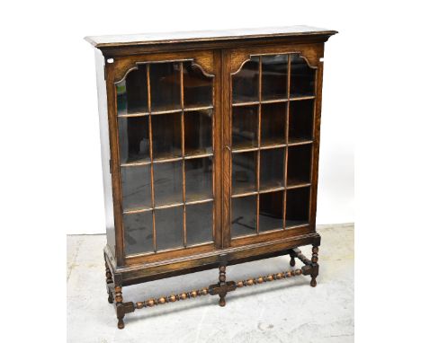 An early 20th century oak two-door glazed display cabinet, raised on bobbin turned and block stretchered supports, 138 x 115 