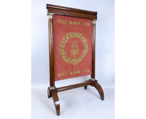 A French Empire mahogany fire screen, with rise and fall tapestry panel, flanked by ormolu capitals, circa 1810, 57 by 33 by 