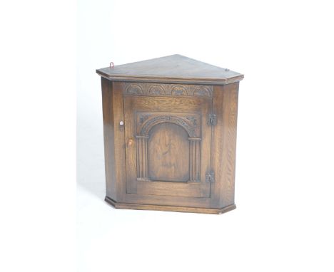 A reproduction oak hanging corner cupboard
With a half roundel frieze above a single panelled door enclosing a single shaped 