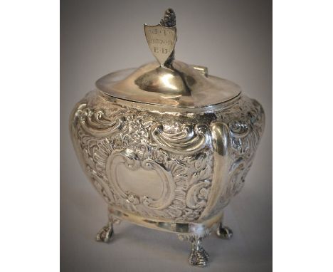 An ornate Edwardian silver tea caddy decorated with flowers and leaves, standing on four ball &amp; claw feet and body having