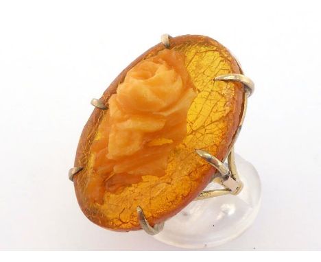 A carved amber dress ring, the oval amber with applied carved amber rose, 3.3cm long, the shank stamped '18ct', finger size R