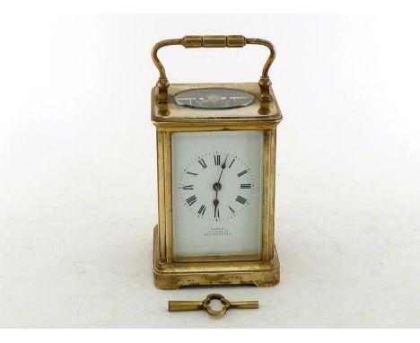 A gilt brass carriage clock with bevelled glass side panels, the white dial with Roman numerals and spade hands, retailer “Ta
