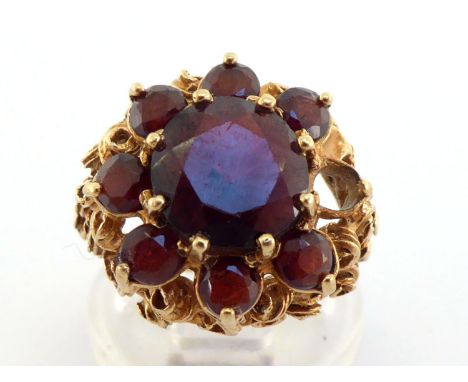 A 1970s 9 carat gold and garnet cluster ring, the central round cut 9.8mm, in a surround of smaller stones (one missing), to 