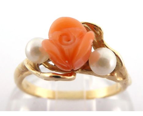 A coral and seed pearl ring, the central carved coral rose between two small seed pearls, mounted in yellow metal, stamped '1