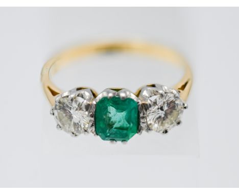 An emerald and diamond ring, centre trap cut emerald of good colour, two modern brilliant cut diamonds (total diamond weight 