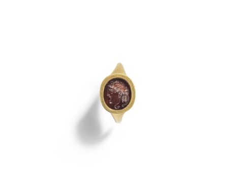  A Roman gold ring with garnet theatre mask intaglio Circa 2nd Century A.D.The hollow gold hoop set with an oval intaglio car