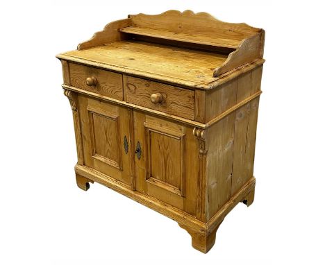 A traditional stripped pine wash stand, raised serpentine back with integral shelf, twin frieze drawers over a cupboard, and 