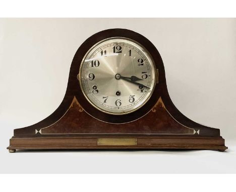 A tambour or ‘Napoleon hat’ form marquetry mantle clock standing on four bun feet, bearing a commemorative brass plaque dated