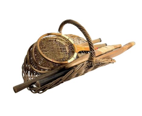 A 1915 wicker flower cutters basket with a collection of early to mid 20th century tennis rackets and cricket bats Gunn and M